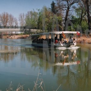 Barco turístico navegando por el río Tajo bajo el puente de entrada al Jardín del Príncipe desde la Vereda de Colmenar, en Aranjuez
