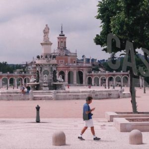 Joven cruzando por la Plaza de San Antonio con la Fuente de Venus (o de la Mariblanca) y la Iglesia de San Antonio al fondo, en Aranjuez