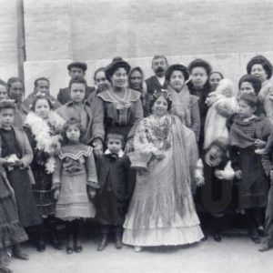 Grupo de hombres, mujeres, niños y niñas alrededor de una niña vestida con un mantón y un traje regional