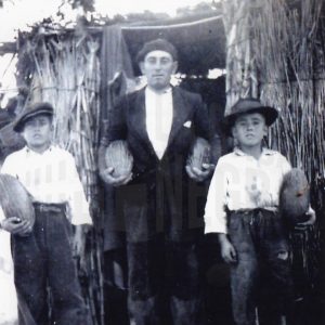 Un hombre y dos niños con melones en sus manos en la puerta de una caseta