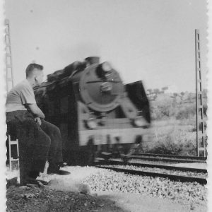 Hombre junto a la vía férrea contemplando el paso de una locomotora de vapor