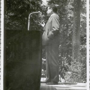 Un señor pronuncia un discurso en un estrado en un jardín