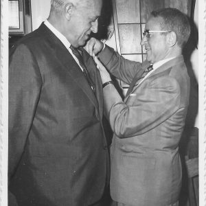 Señor condecorando a otro con una insignia en el pecho.