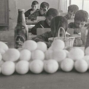 Retrato de alumnos en sus pupitres con varias docenas de huevos y dos botellas de cristal en primer plano