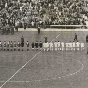 Árbitros y jugadores de dos equipos de fútbol colocados en línea en el Estadio Santiago Bernabéu durante la actuación de una banda de música