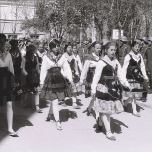 Varias chicas con trajes regionales desfilan ante soldados en formación