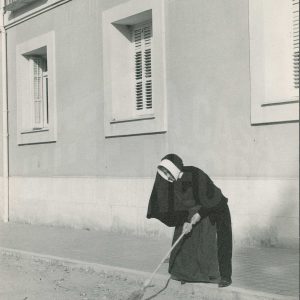 Una monja barriendo la calle del Príncipe frente a la puerta del colegio Sagrada Familia de Aranjuez