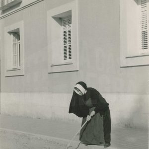 Una monja barriendo la calle del Príncipe frente a la puerta del colegio Sagrada Familia de Aranjuez