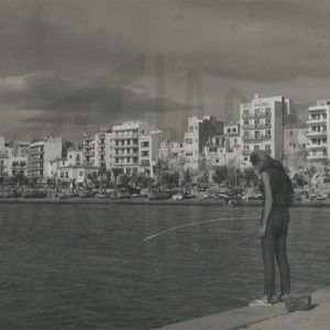 Una mujer pesca con una caña en el mar junto a una localidad costera