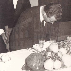 Un señor ayuda a sentarse al Príncipe Juan Carlos de Borbón antes de una comida con motivo de su visita a la fábrica de MAFE en Aranjuez
