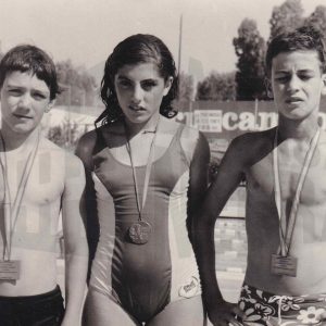 Maribel Talavera Gálvez junto a otros dos niños en una piscina, todos ellos con medallas