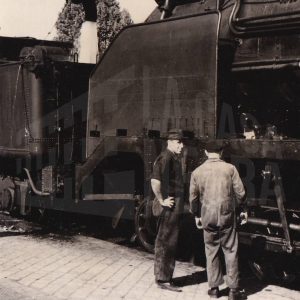 Dos operarios junto a una locomotora de carbón mientras reposta de agua