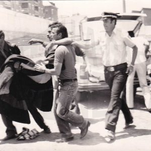 Dos hombres trasladan a un deportista herido o lesionado acompañados por un policía municipal en el Campo Municipal de Deportes de Aranjuez