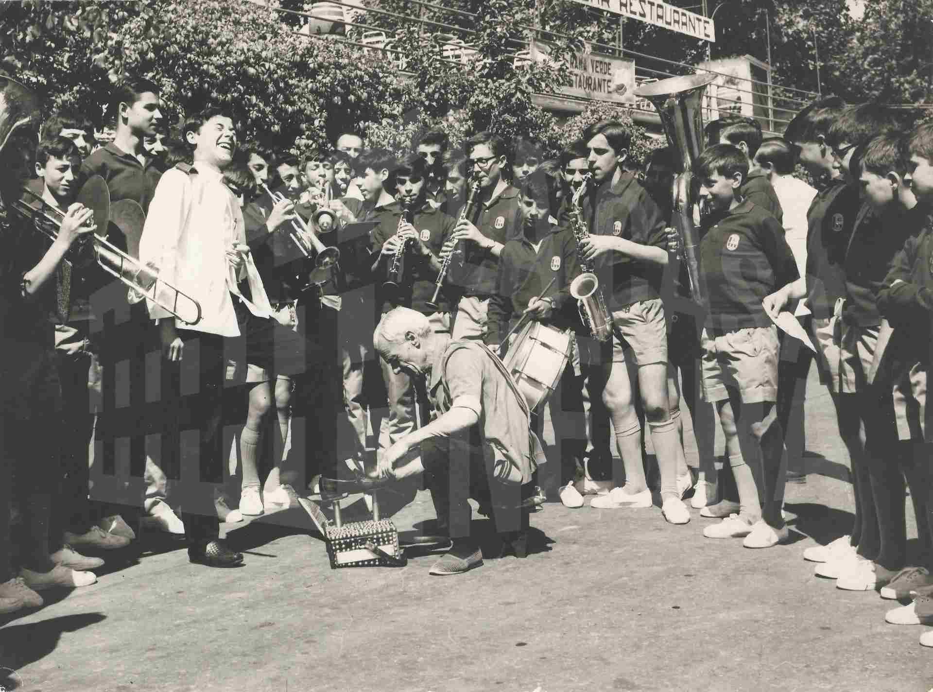 Banda musical formada por niños de Bilbao tocan sus instrumentos alrededor de un limpiabotas en Aranjuez