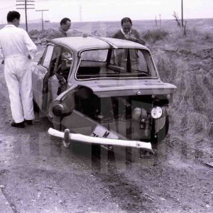 Tres personas observan un coche accidentado en una cuneta