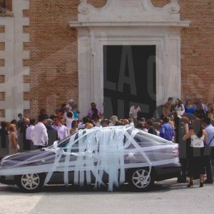 Numerosas personas y el coche de los novios en la puerta de la Iglesia de Alpajés en Aranjuez