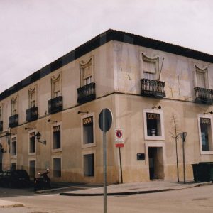 Edificio en la esquina de las calles Abastos y Stuart en Aranjuez con el portalón de entrada a una corrala, un banco y varios comercios