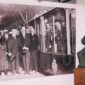 Busto del marqués de Salamanca junto a una fotografía mural de la exposición por el 150 Aniversario de la línea ferroviaria Madrid-Aranjuez en Aranjuez en la que aparecen el rey Alfonso XIII y otras personas durante la inauguración de la primera línea de Metro de Madrid
