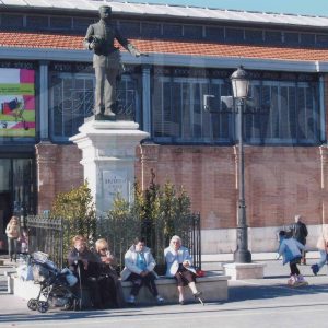 Varias personas alrededor de la puerta del Mercado de Abastos y de la estatua de Alfonso XII en la Plaza de la Constitución de Aranjuez